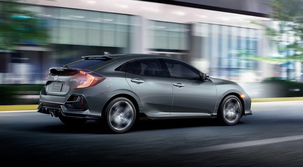 A grey 2020 Honda Civic Hatchback Sport Touring is shown from the side driving through a city at night.