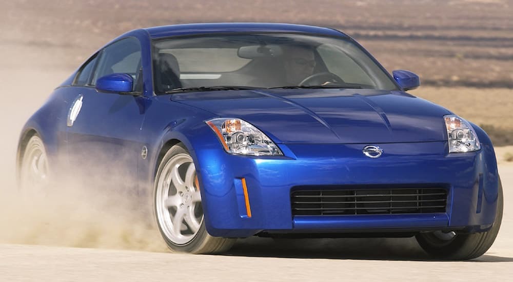 A blue 2007 Nissan 350z is shown from the front while it drifts in dirt.