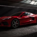 A red 2021 Chevy Corvette C8 is shown from the side at an angle in a dark warehouse after leaving a pre-owned C8 Corvette dealership.