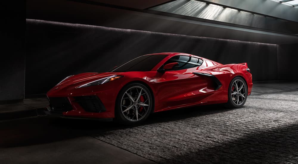 A red 2021 Chevy Corvette C8 is shown from the side at an angle in a dark warehouse after leaving a pre-owned C8 Corvette dealership.