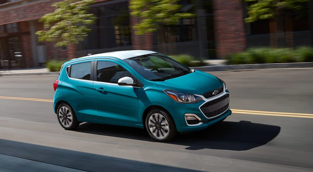 A teal 2022 Chevy Spark is shown from the side as it drives down a city street.