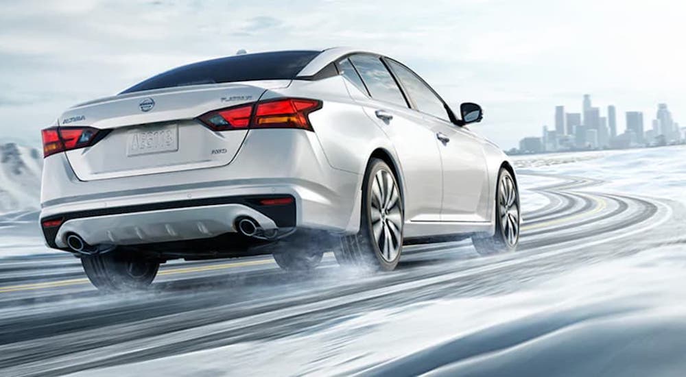 A white 2021 Nissan Altima is shown from behind while driving down a snow covered road.