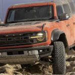 An orange 2022 Ford Bronco is shown off-roading after researching 2022 Ford Bronco sales.