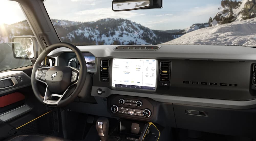 The black interior of a 2022 Ford Bronco shows the steering wheel and infotainment screen.