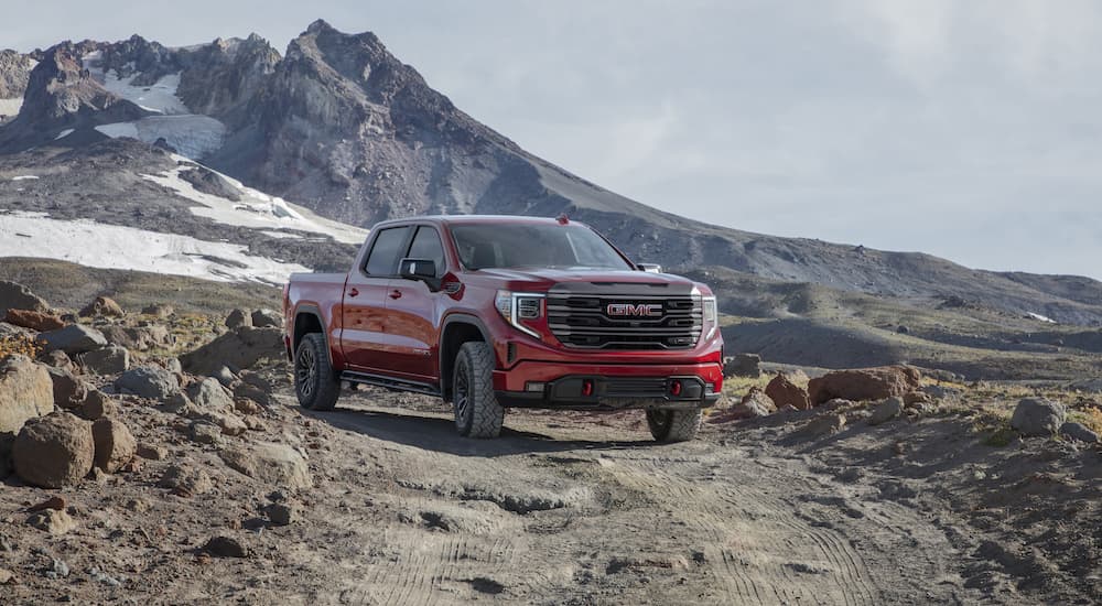 A red 2022 GMC Sierra AT4X is shwon from the front at an angle while driving on a dirt trail in the mountains.