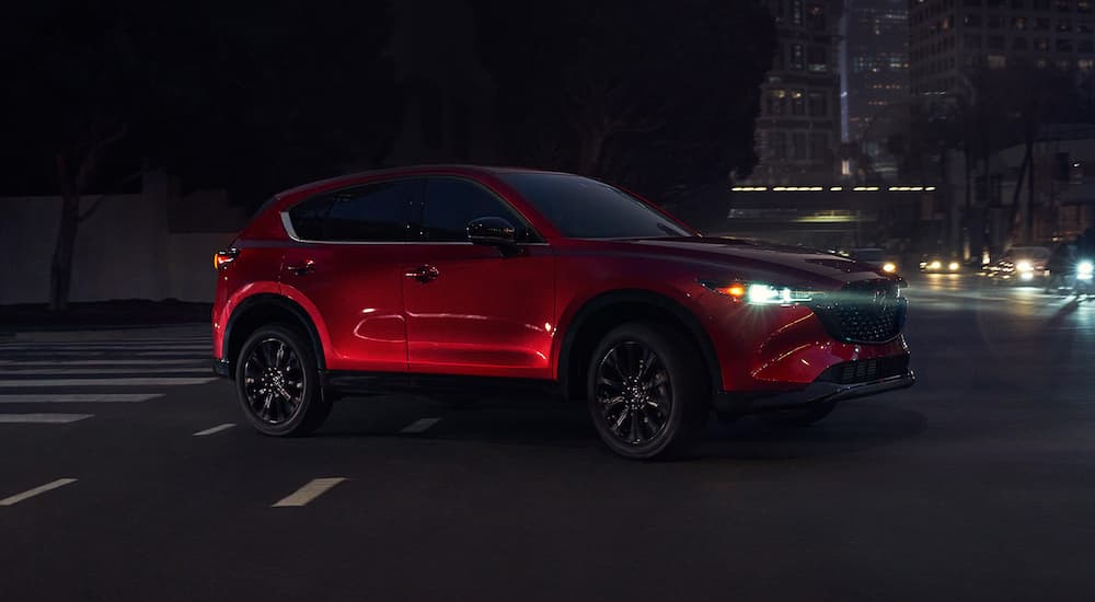 A red 2022 Mazda CX-5 is shown driving on a city street at night.