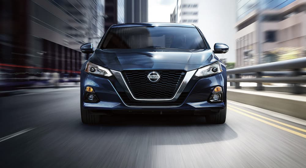 A blue 2022 Nissan Altima is shown from the front driving on an open road during a 2022 Nissan Altima vs 2022 Subaru Legacy comparison.