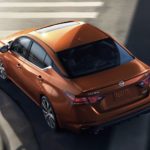 An orange 2022 Nissan Altima is shown from above rounding a city corner.