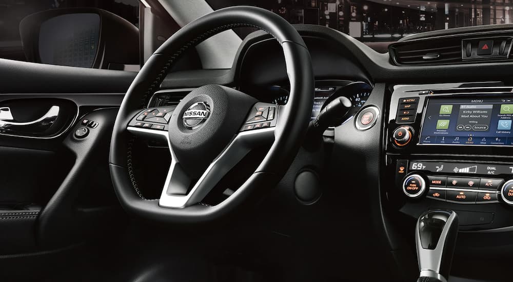 The black interior of a 2022 Nissan Rogue Sport shows the steering wheel and infotainment screen.