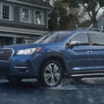 A blue 2022 Subaru Ascent Touring is shown from the side driving past a house in the rain.