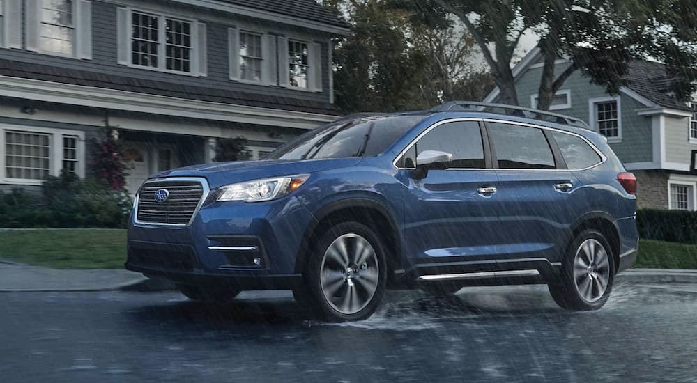 A blue 2022 Subaru Ascent Touring is shown from the side driving past a house in the rain.