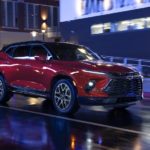 A red 2023 Chevy Blazer RS is shown driving on a wet city street at night.