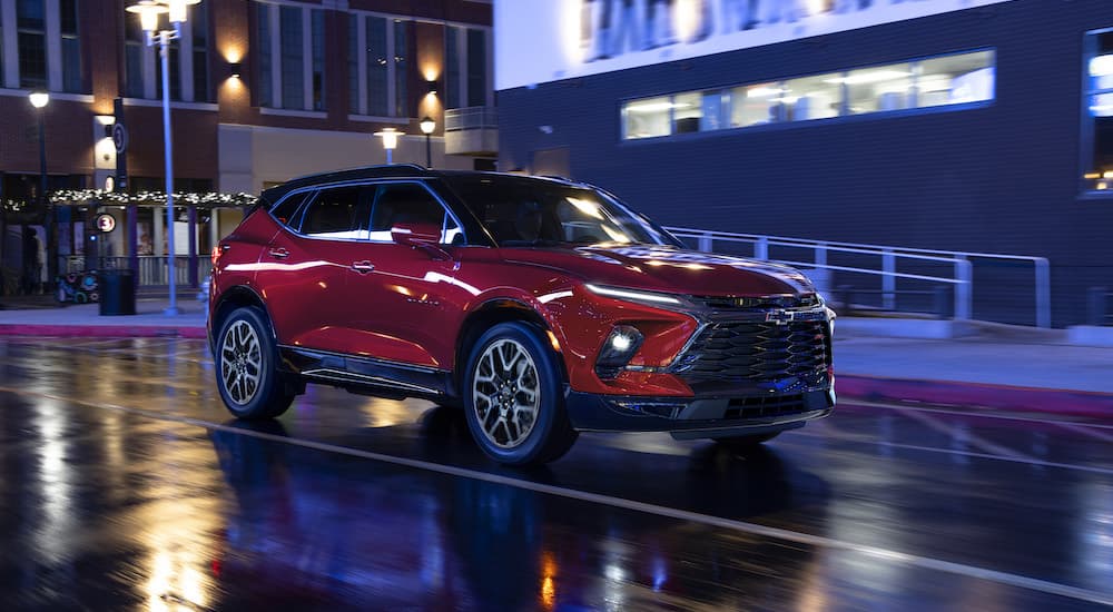 A red 2023 Chevy Blazer RS is shown driving on a wet city street at night.