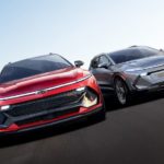 A red and a silver 2024 Chevy Equinox EV are both shown from the front on a racetrack.