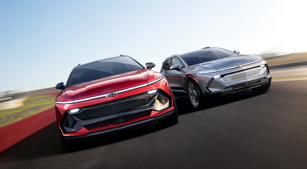 A red and a silver 2024 Chevy Equinox EV are both shown from the front on a racetrack.