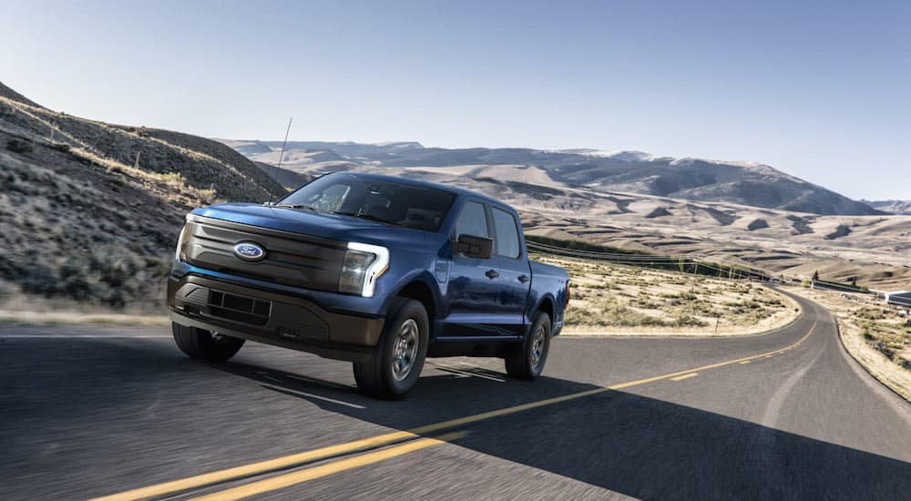 A blue 2022 ford F-150 Lightning is shown from the front at an angle driving on an open road.
