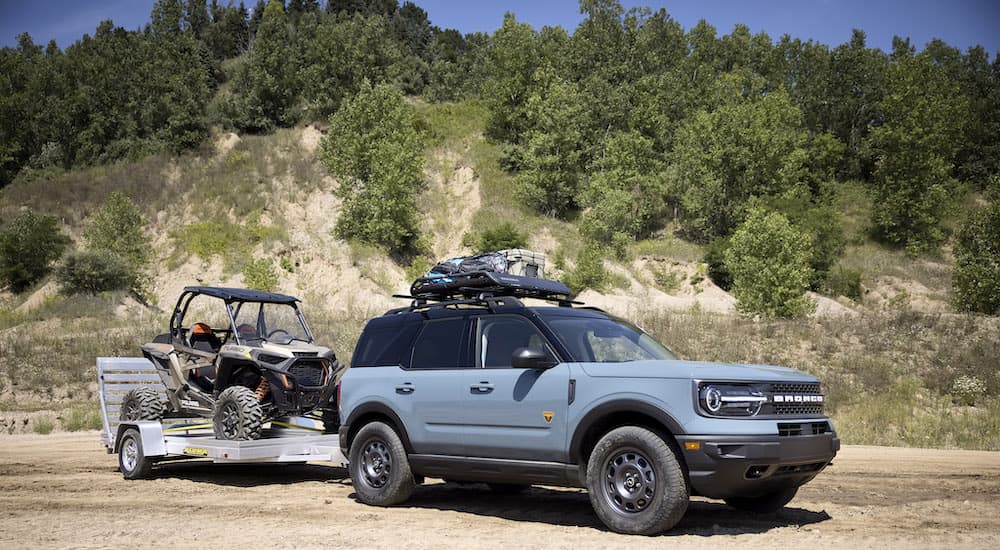 A grey 2022 Ford Bronco Sport is shown from the side towing a Polaris Razor off-road.