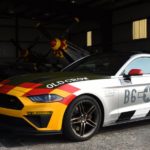 A 2020 Ford Mustang Roush 'Old Crow' is shown from the side at an angle in front of a hanger with P51 Mustang fighter planes inside.