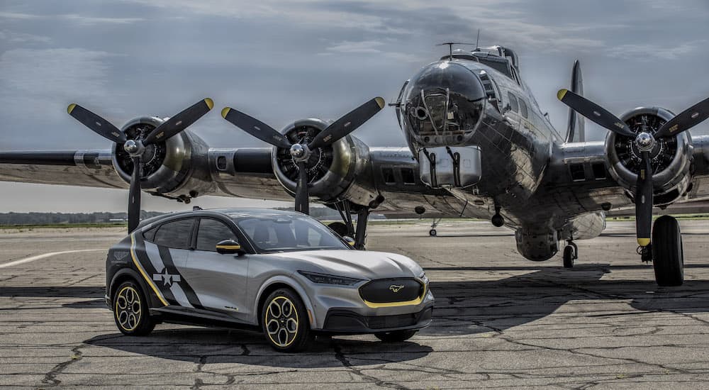 A silver 2020 Ford Mustang Mach-E is shown from the side in front of a B17 Flying Fortress after the owner searched 'used Ford for sale'.