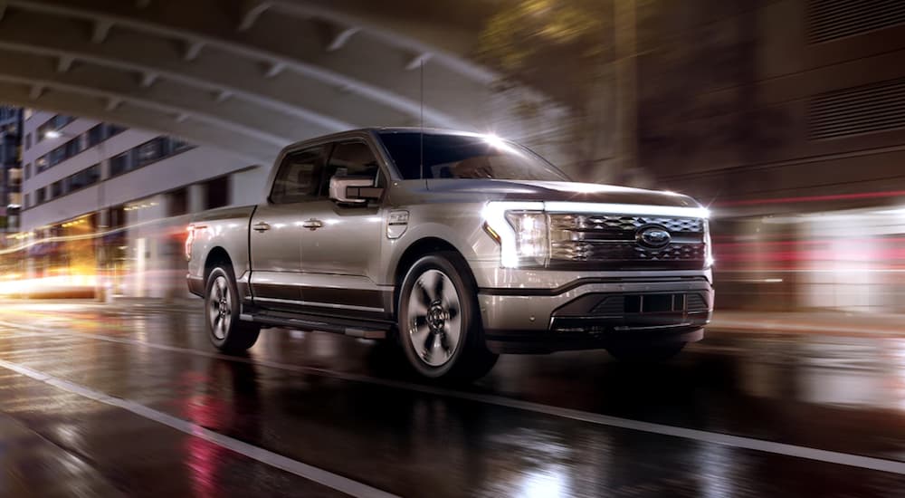 A grey 2022 Ford F-150 Lightning is shown driving through a city at night.