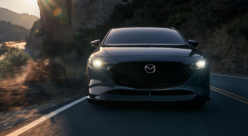 A dark grey 2022 Mazda3 is shown driving on a mountain road after visiting a Mazda dealer.