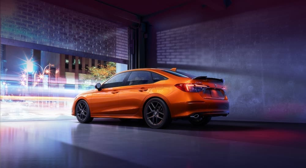 An orange 2022 Honda Civic SI is shown from the rear at an angle exiting a parking garage in a city.