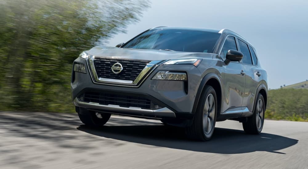 A grey 2022 Nissan Rogue is shown from the front at an angle while it drives down the road.