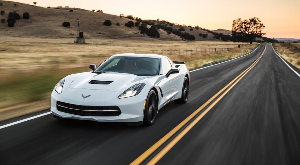A white 2016 Chevy Corvette Stingray is shown from the front at an angle while driving on an open road.