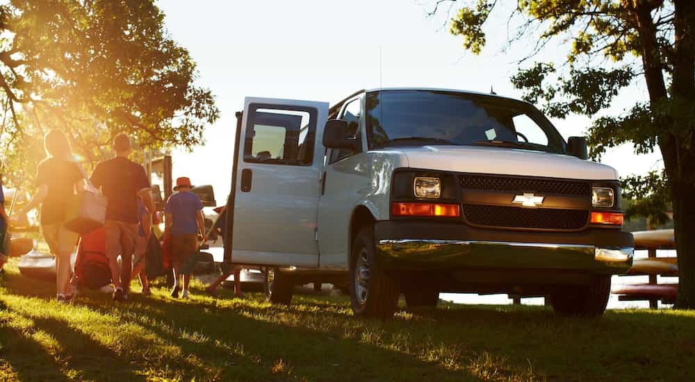 A white 2016 Chevy Express van is shown from the front while a family unloads cookout supplies.