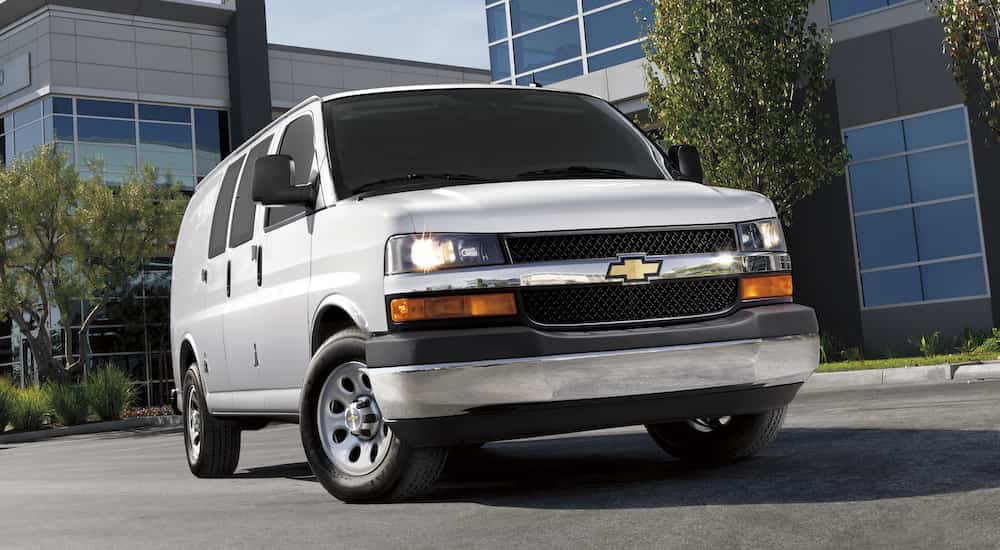 A white 2016 Chevy Express van is shown from the front at an angle parked near a building.