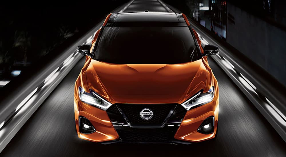 An orange 2021 Nissan Maxima is shown from the front on a dark road after leaving a Charlotte used car dealership.