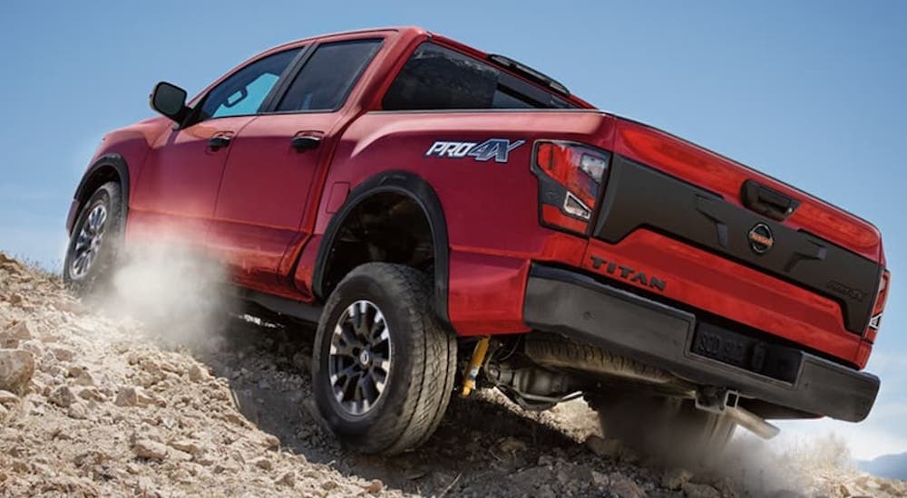 A red 2022 Nissan Titan Pro-4x is shown from the rear at a low angle while it crawls over rocks.