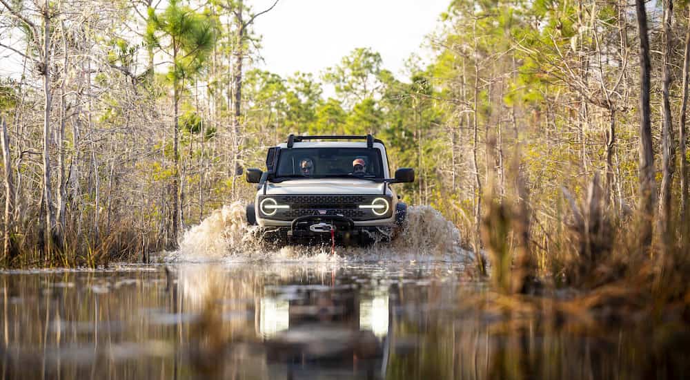 A 2022 Ford Bronco Everglades is shown from the front as it drives through mud at speed.