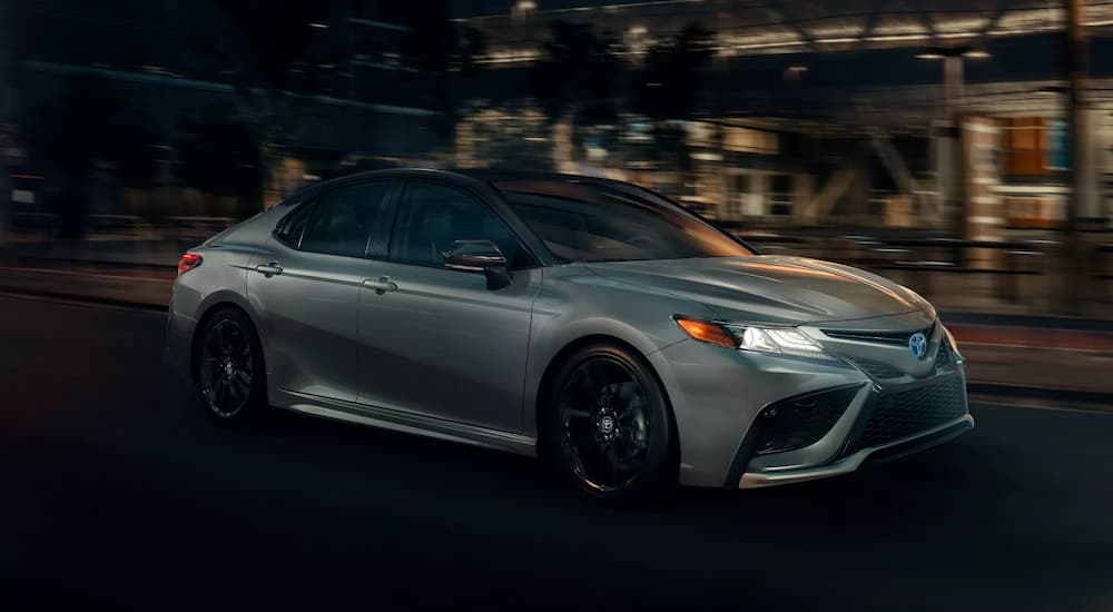 A silver 2022 Toyota Camry XSE Hybrid is shown driving on a city street at night.