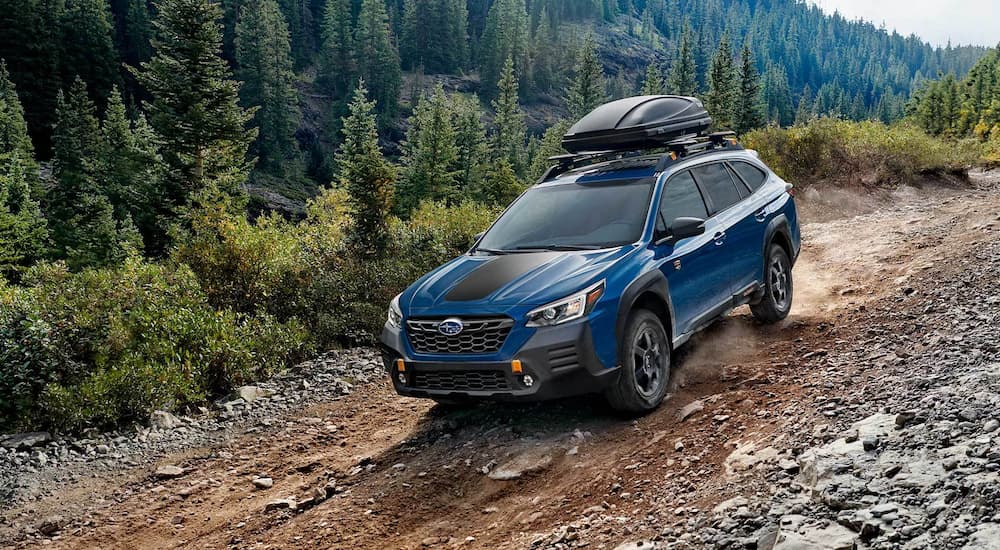 A blue 2022 Subaru Outback Wilderness is shown driving down a dirt trail.