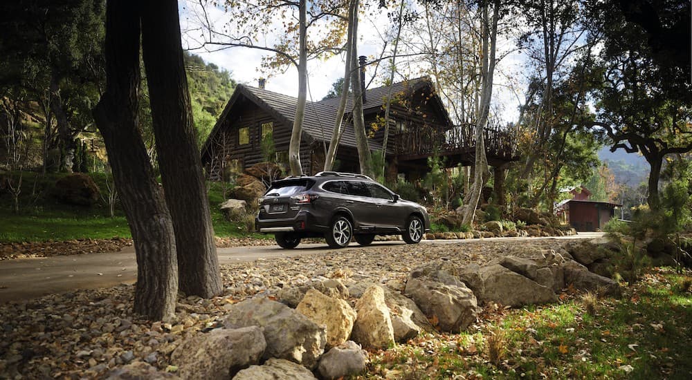 A dark grey 2022 Subaru Outback XT is shown parked outside a cabin in the woods.