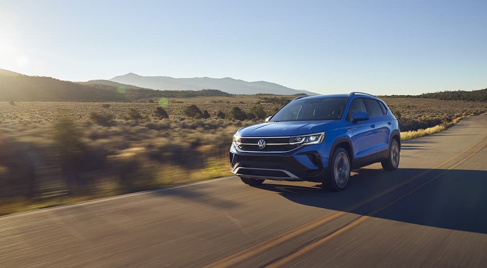 A blue 2022 Volkswagen Taos is shown from the front driving on an open road.