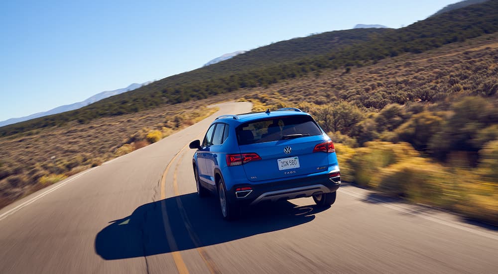 A blue 2022 Volkswagen Taos is shown from the rear driving on an open road during a 2022 Volkswagen Taos vs 2022 Buick Encore GX comparison.