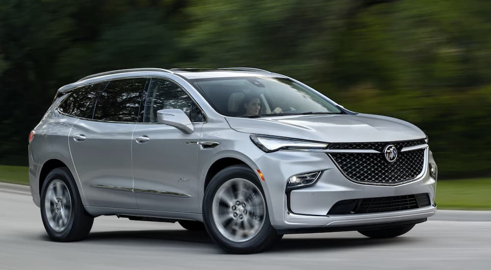 A silver 2022 Buick Enclave is shown from the side driving on a tree lined road after leaving a Buick dealer near you.