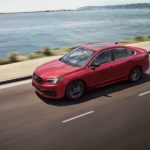 A red 2021 Subaru Legacy is shown from the side driving on an open road past a body of water.