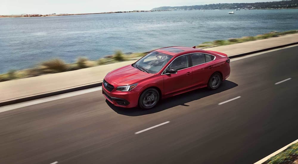 A red 2021 Subaru Legacy is shown from the side driving on an open road past a body of water.