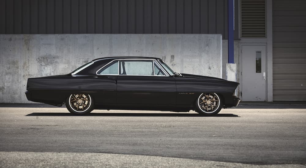 A black 1967 Chevy Nova is shown from the side outside of a warehouse.