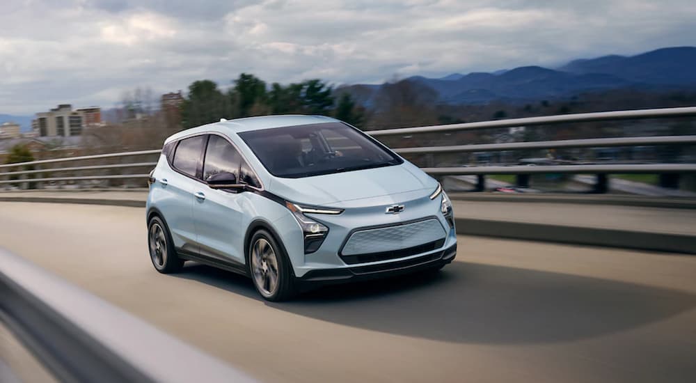 A blue 2022 Chevy Bolt EV is shown from the front driving on a bridge after leaving a Chevy dealer.