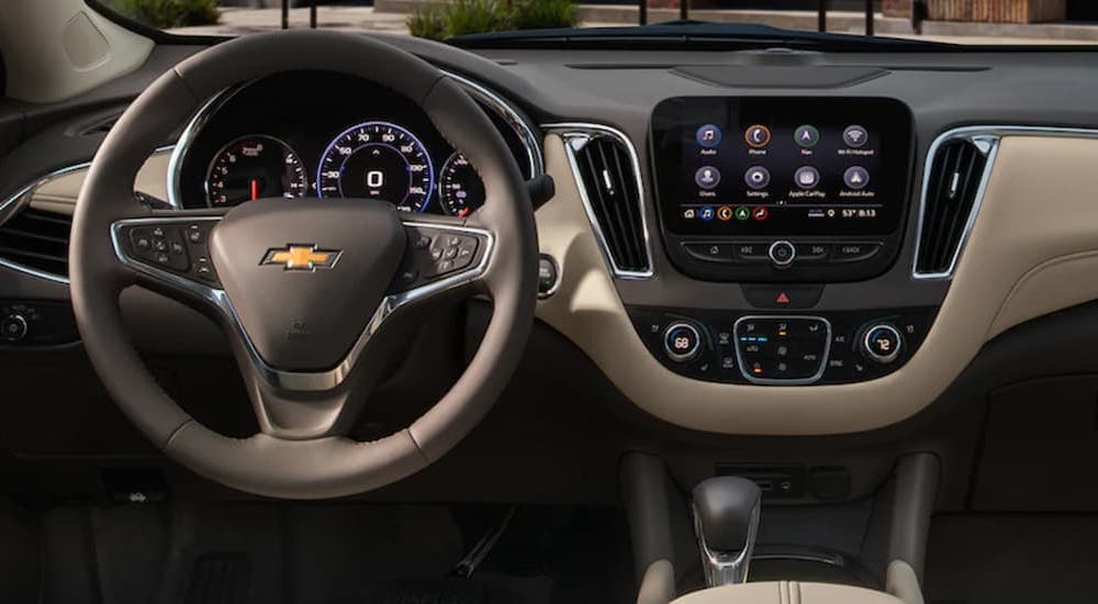 The black and grey interior of a 2022 Chevy Malibu shows the steering wheel and infotainment screen.