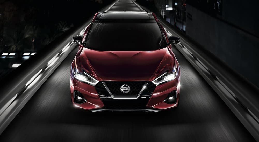 A red 2021 Nissan Maxima is shown from the front driving on an open road at night.