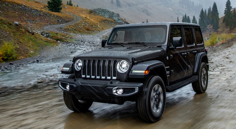 A black 2018 Jeep Wrangler Unlimited is shown driving on a wet trail.