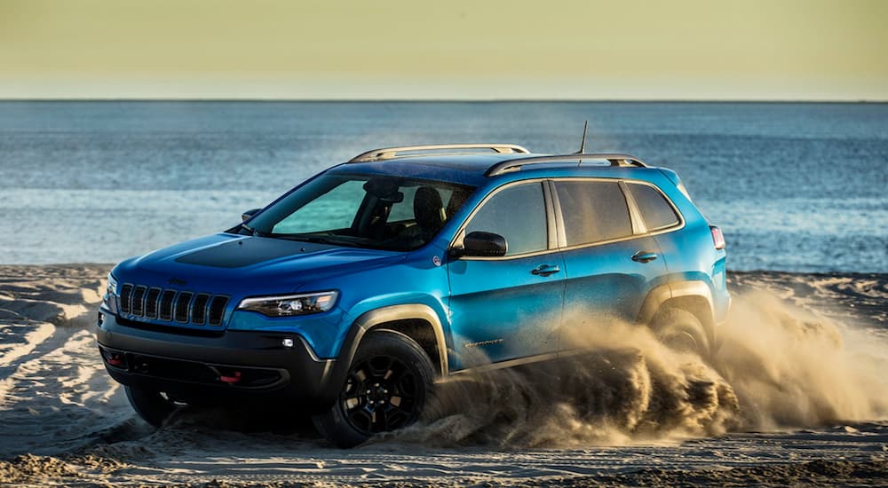 A blue 2022 Jeep Cherokee Trailhawk is shown from the front at an angle while it drives on a beach.