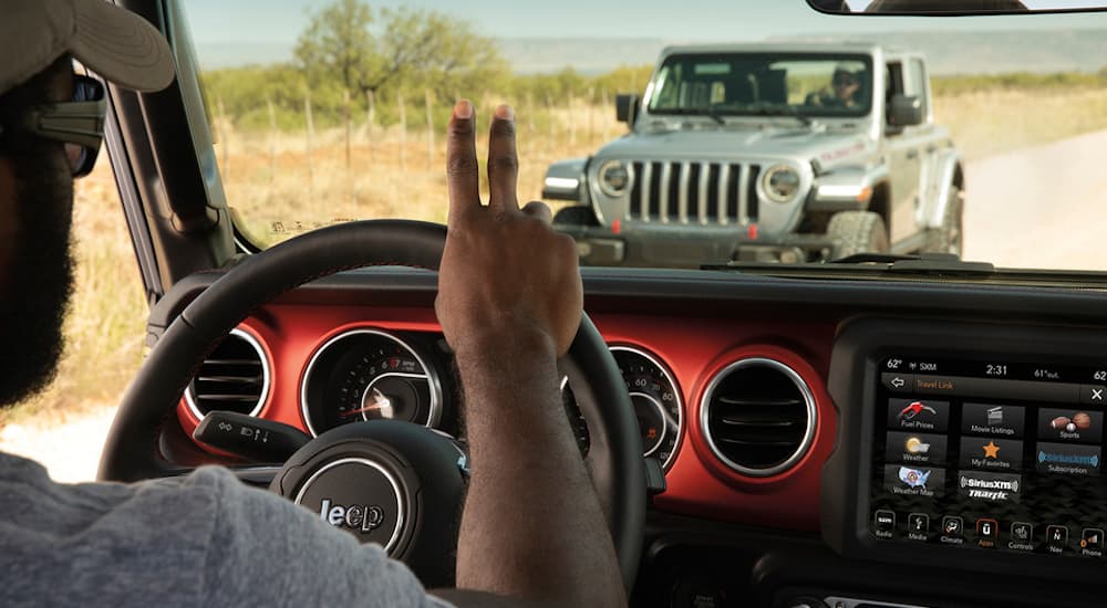 A person in a 2022 Jeep Gladiator is shown waving at a silver 2022 Jeep Gladiator.