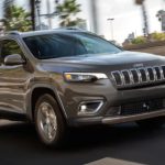 A grey 2022 Jeep Cherokee is shown from the front at an angle while it drives down the street.