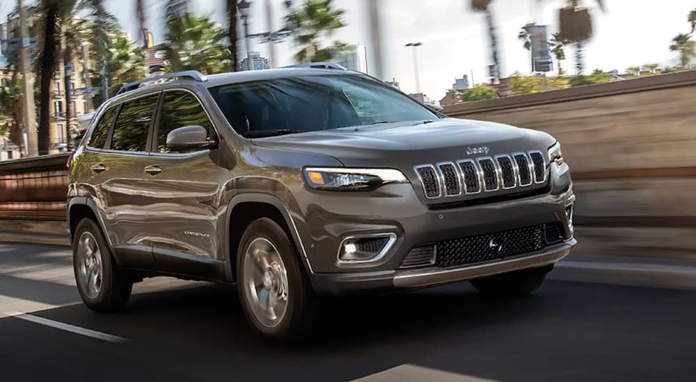 A grey 2022 Jeep Cherokee is shown from the front at an angle while it drives down the street.